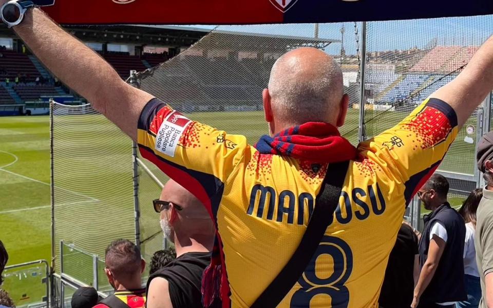 Un tifoso con la maglia del Lecce alza una sciarpa del Cagliari sugli spalti dello stadio.